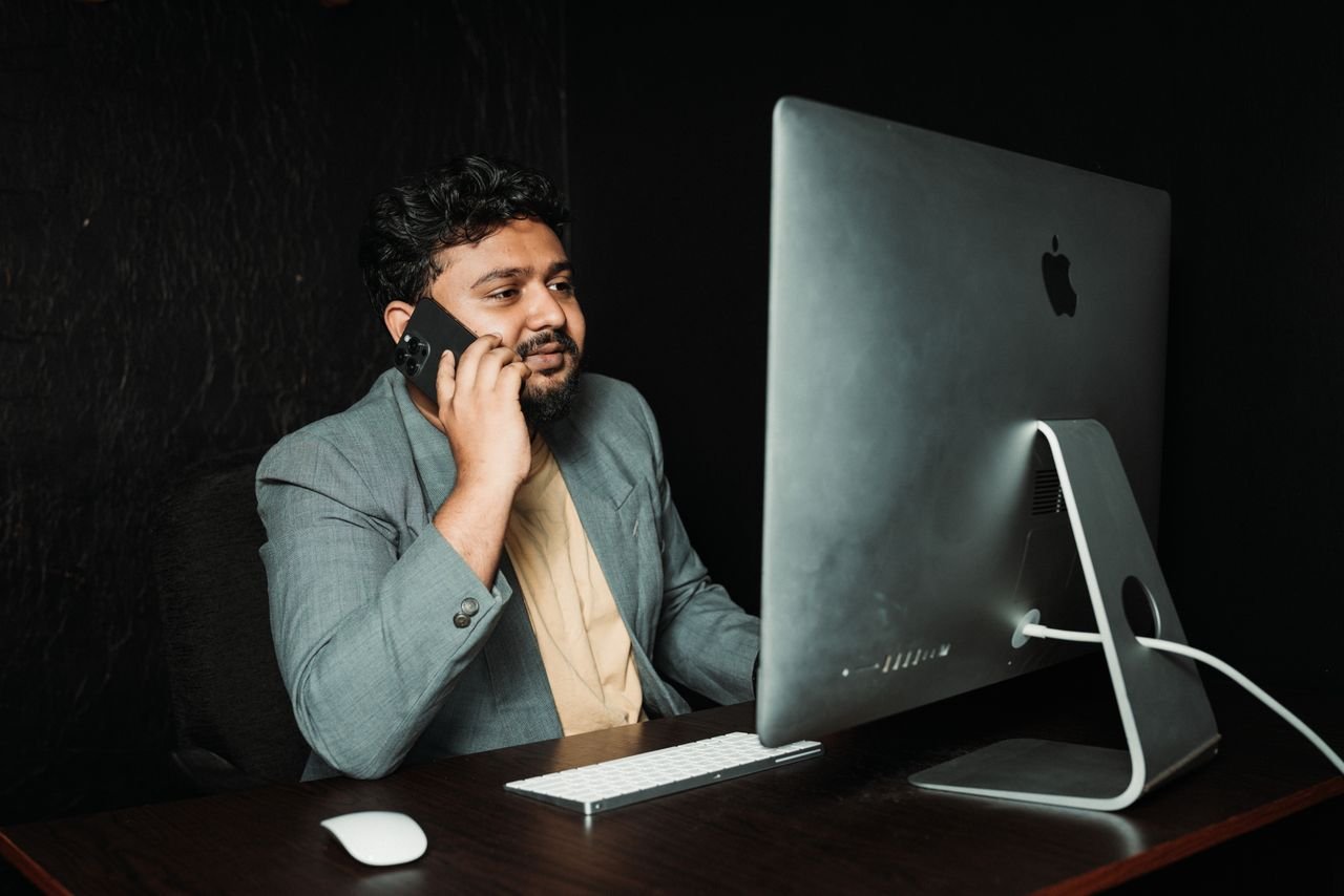 Our Services Professional man multitasking at office desk using computer and smartphone.