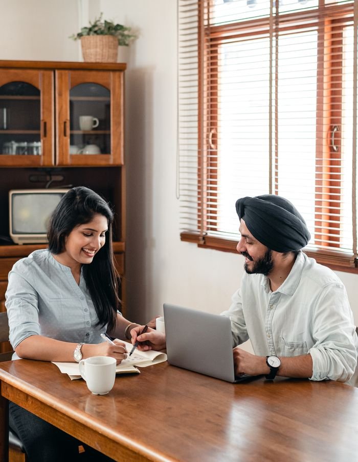 About From above of positive young Indian man and woman in casual wear doing assignment together at home using laptop